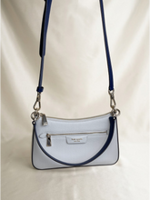 Load image into Gallery viewer, A light blue pebbled leather crossbody handbag with navy blue trim and strap, featuring silver-tone hardware and a small gold 'kate spade new york' logo plaque on the front.